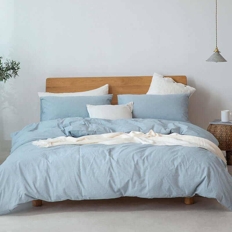 Japanese style Muji-style bedding in soft blue, featuring duvet cover and pillows on a wooden bed.