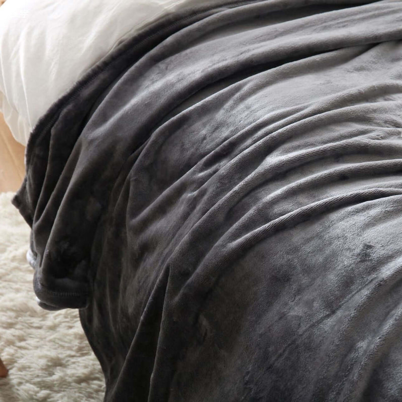 Cozy dark gray flannel coral fleece blanket draped over a bed, ideal for air conditioning comfort.