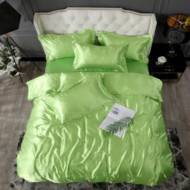 Luxurious green silk bedding set with pillows and a decorative palm leaf on a stylish bed.