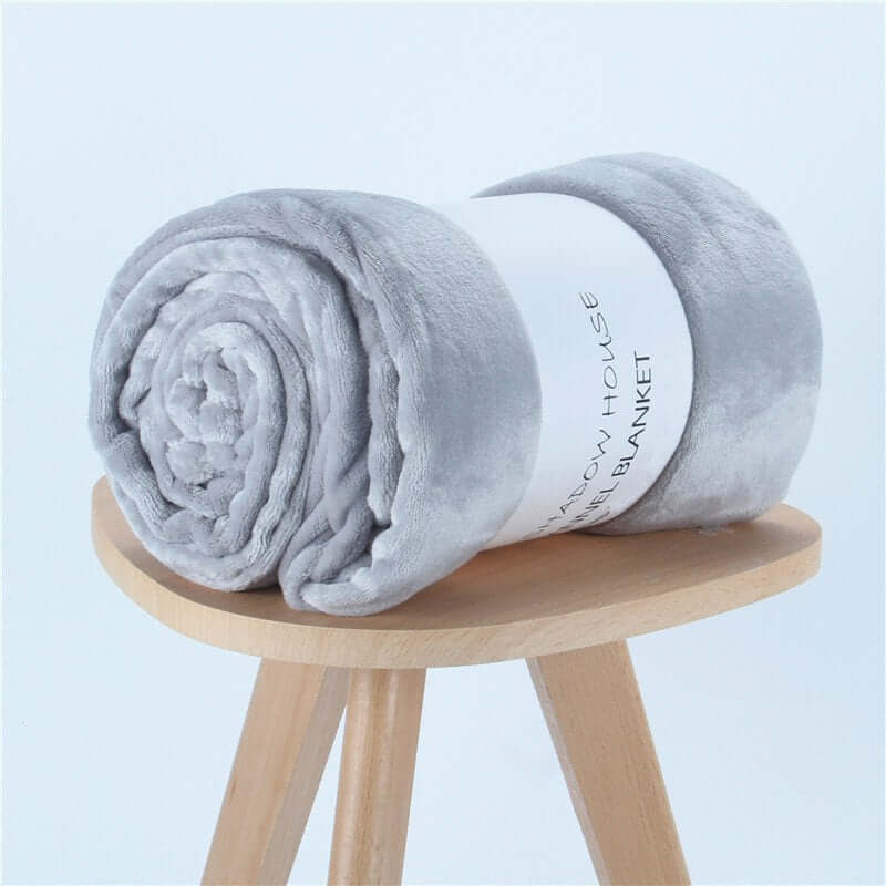 Rolled gray flannel coral fleece blanket on a wooden stool, perfect for air-conditioning and cozy naps.