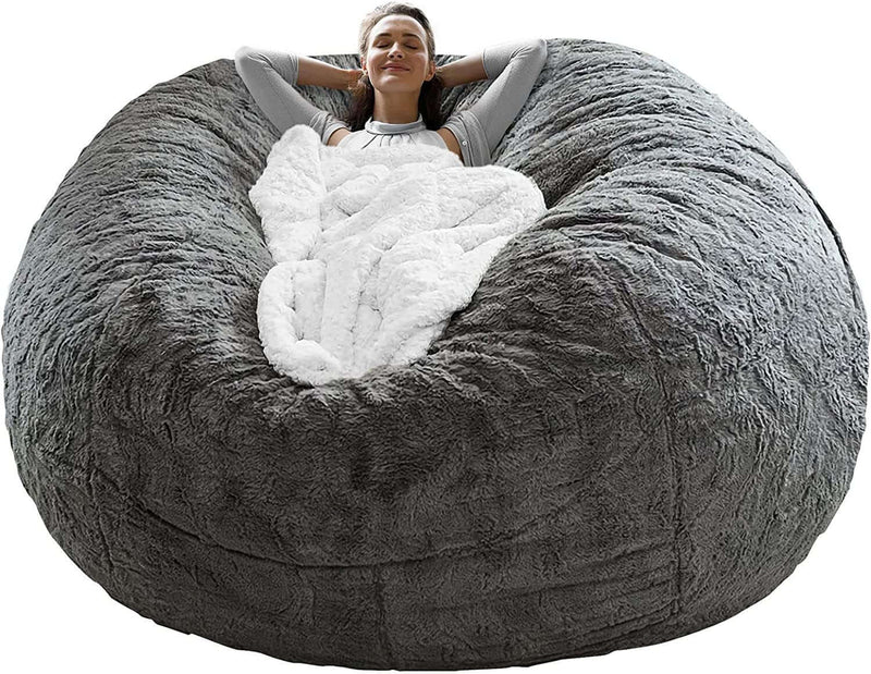 Cozy woman relaxing on a big round soft fluffy dark grey bean bag chair cover with a blanket.