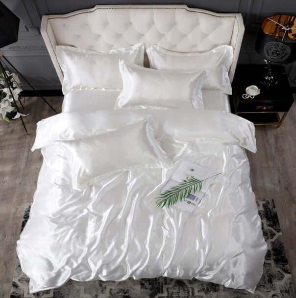 Elegant white silk bed sheet quilt cover with matching pillows in a luxurious bedroom setting.